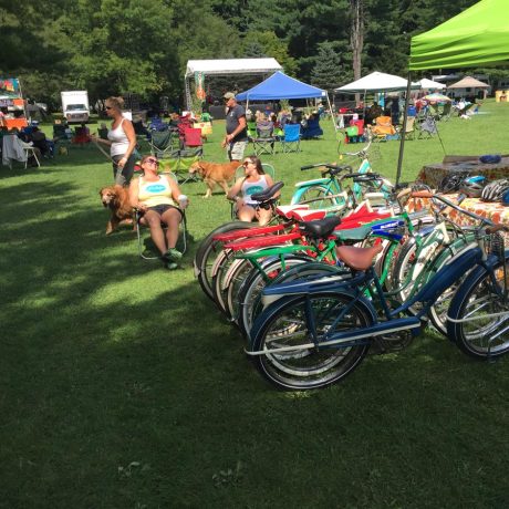 wide shot of bicycles, people sitting in covered shaded areas, and a woman walking dogs