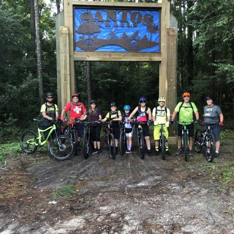 people smiling on bicycles under sign